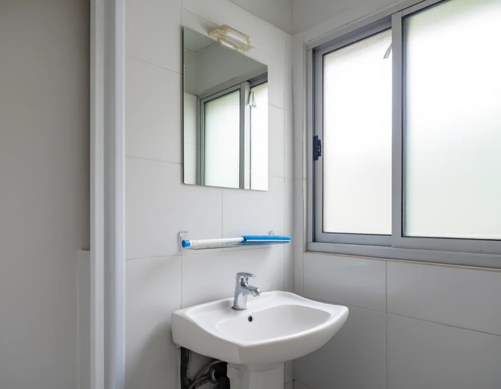 A small plain white-tiled bathroom with a clean basin, mirror and frosted window in flat daylight